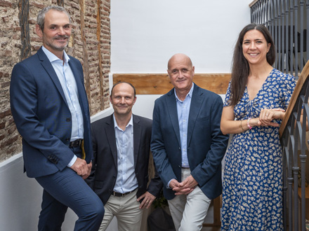 3 hommes et 1 femme montent escalier, mur de briques et poutres